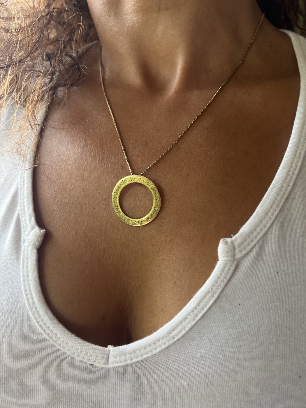 The gold circle necklace worn on a fine chain over a white top